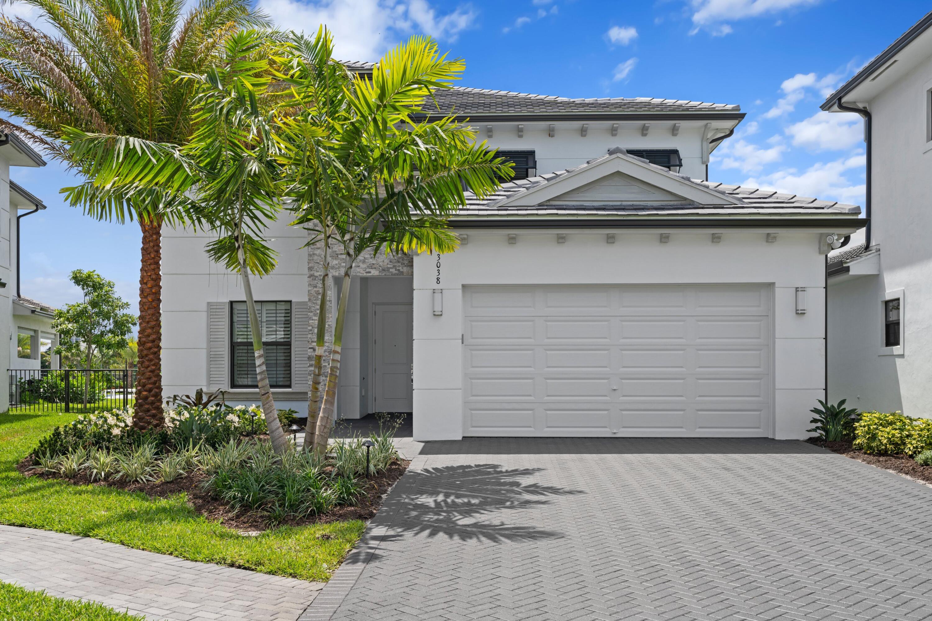 White modern home with a double garage, palm trees, and a wide paved driveway.