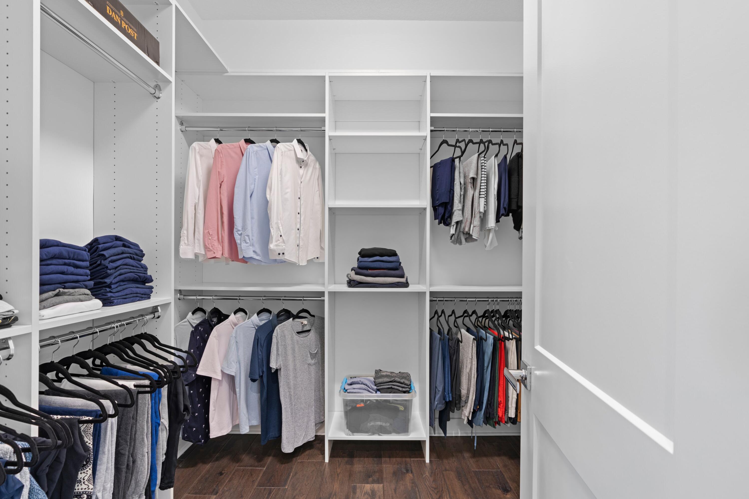 Walk-in closet with built-in shelving, hanging clothes, folded garments, and dark wood flooring.