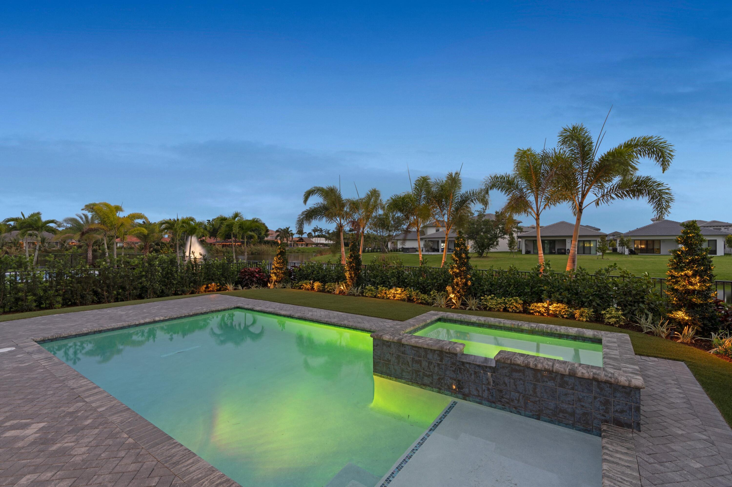 Backyard pool and raised spa with palms, landscaped grounds, and a lake fountain beyond the fence.