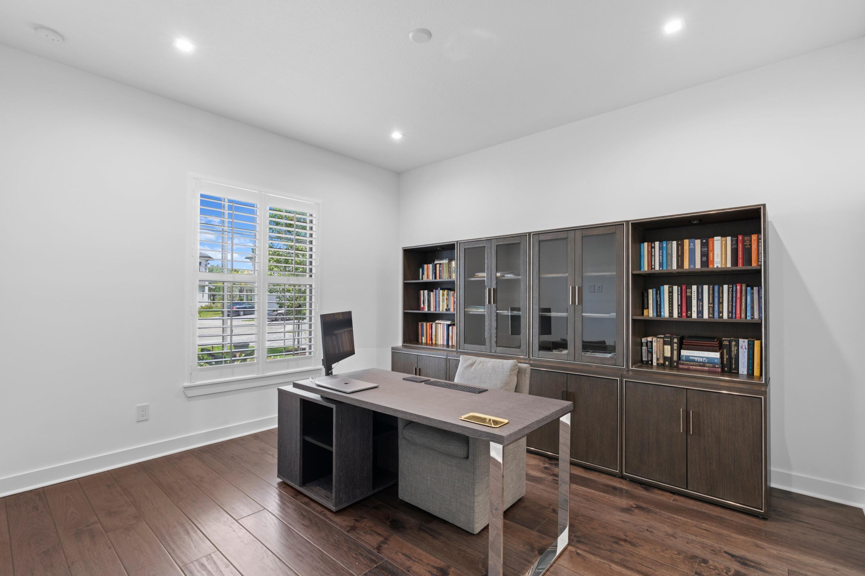 Home office with built-in bookcases, a dark wood desk, and a shuttered window.