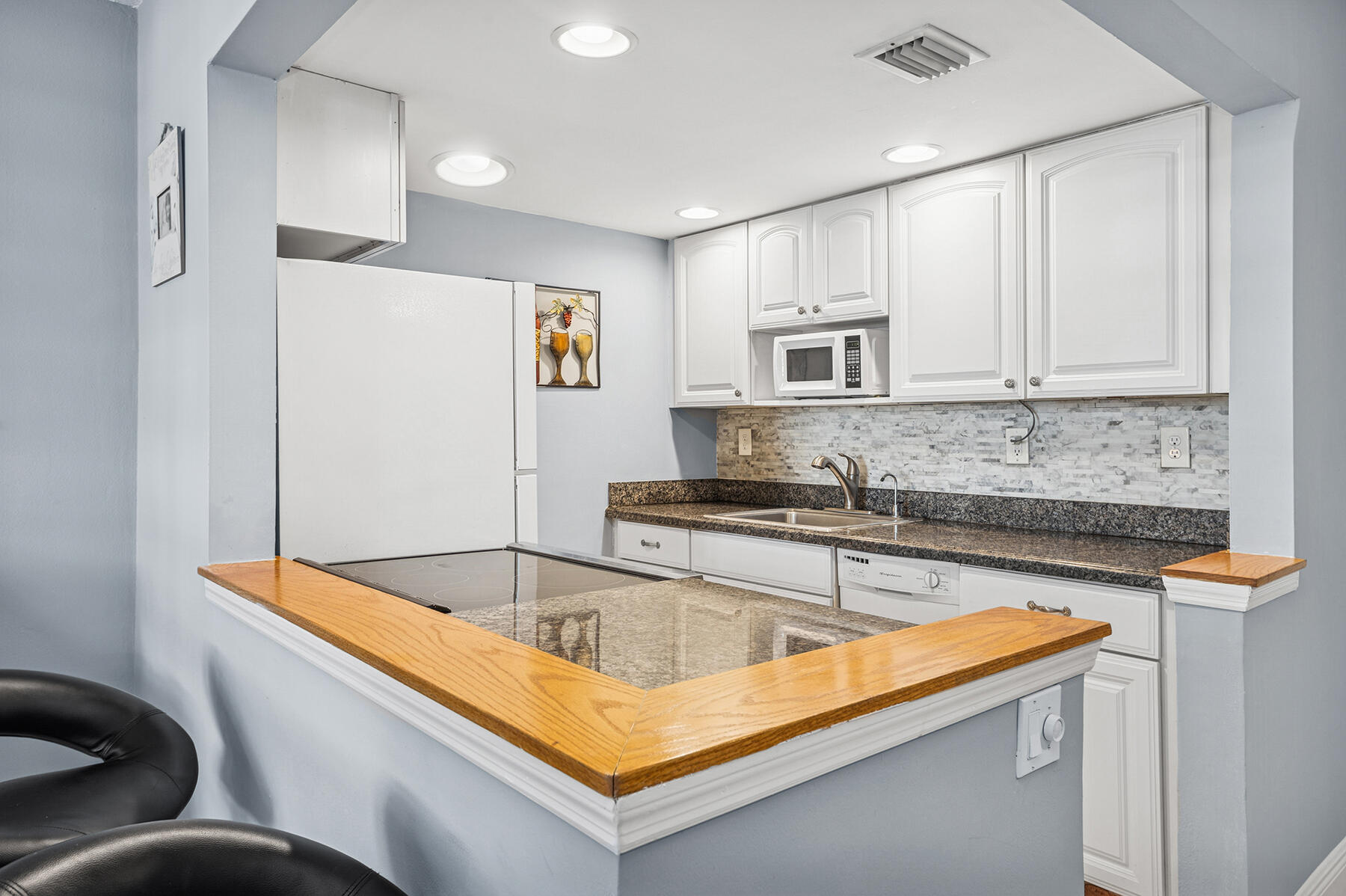 Kitchen with white cabinets, granite counters, mosaic backsplash, and a wood-trimmed breakfast bar.