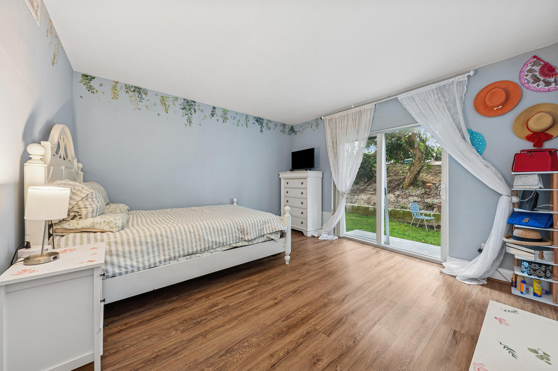 Bedroom with a white bed, sheer-curtained sliding door, and garden visible outside.