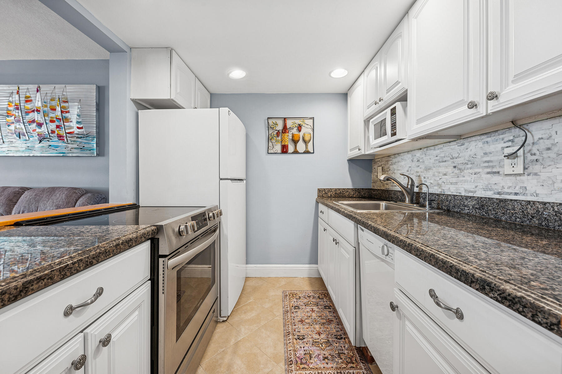 Galley kitchen with white cabinets, granite counters, and stainless steel range beside an adjoining living area.