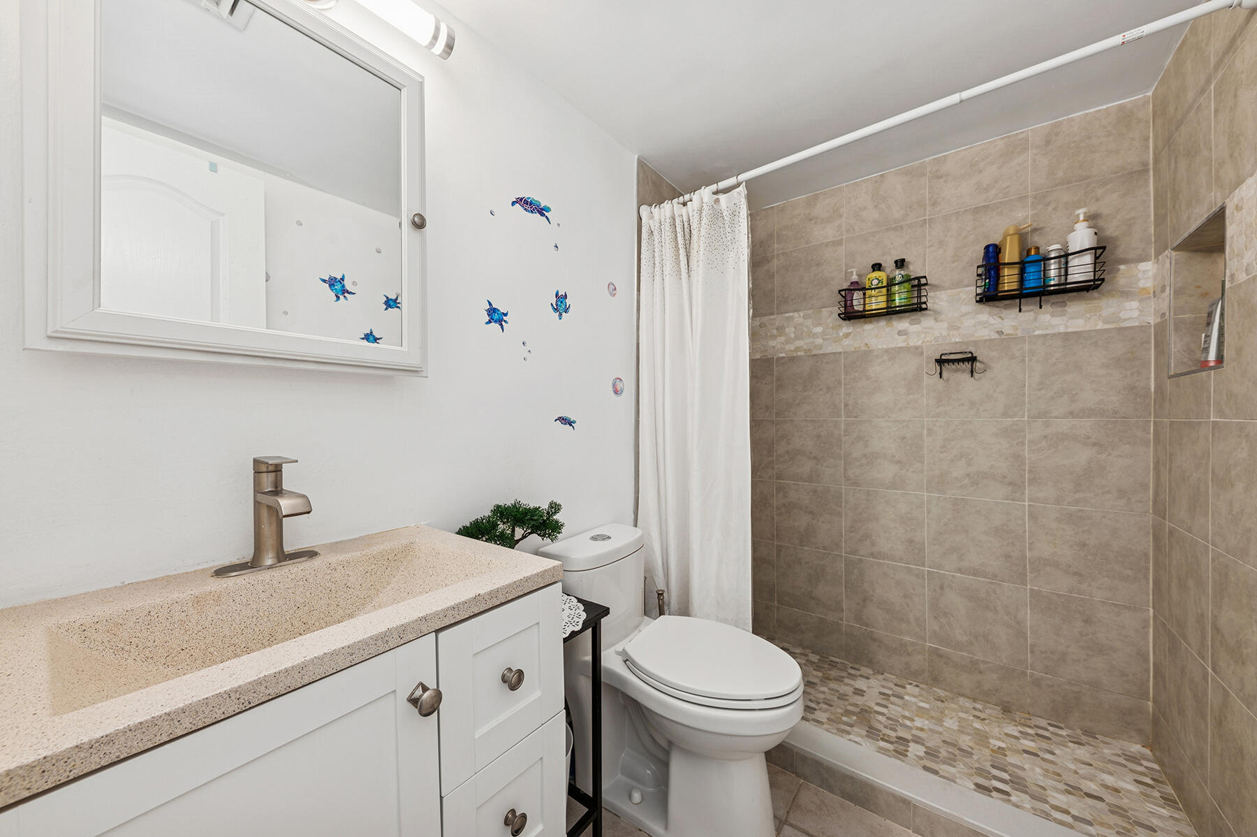 Bathroom with a beige-countertop vanity, tiled shower, pebble-mosaic floor, and blue sea turtle decals.
