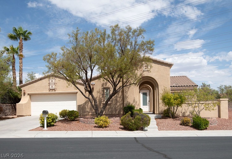 Tan stucco home with an arched entry, attached garage, and desert landscaping.