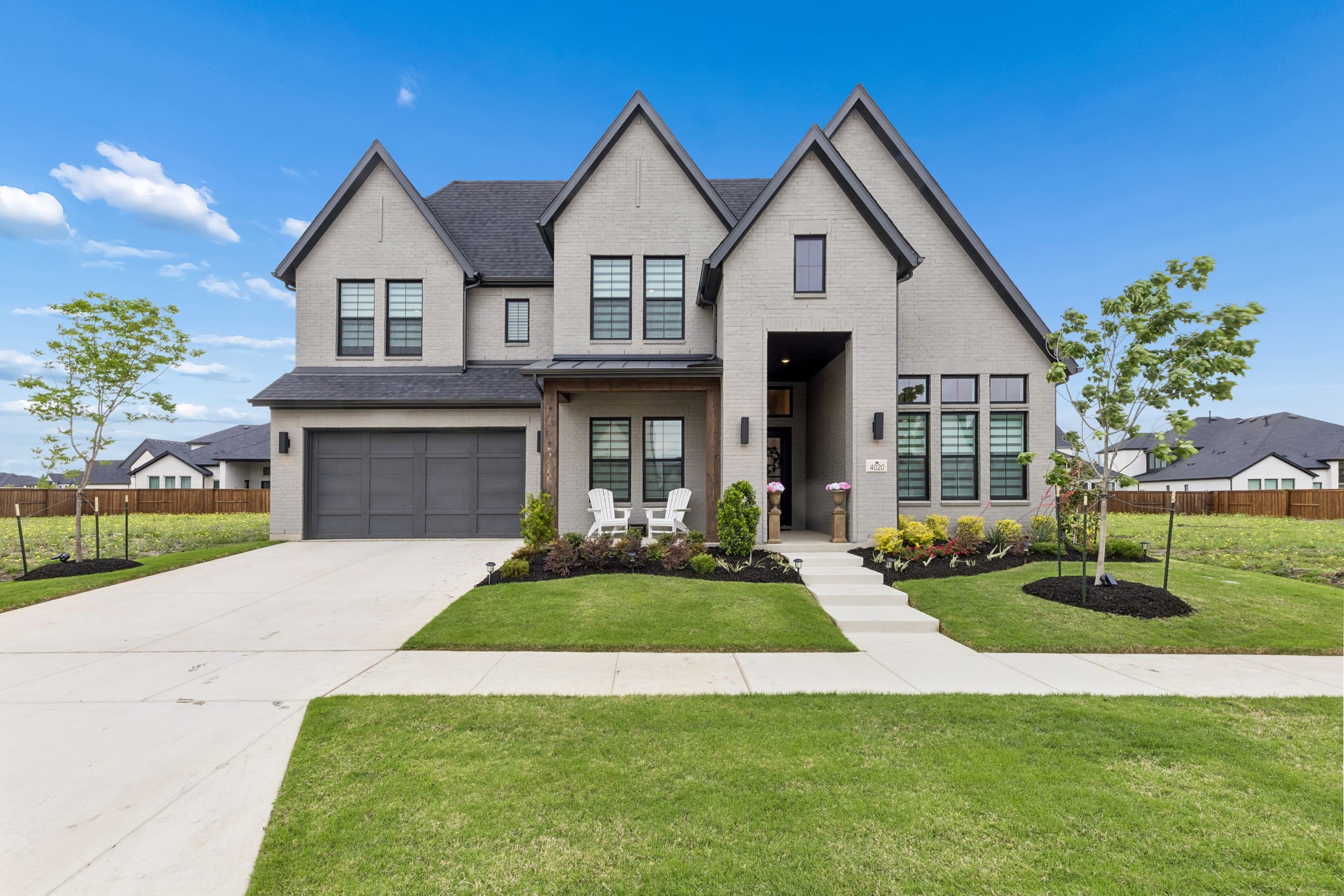 Two-story light brick house with steep gables, a dark double garage, and landscaped front yard.
