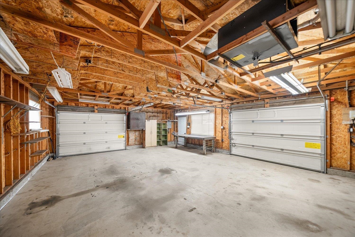 Unfinished garage with exposed roof trusses, two overhead doors, and a worktable.