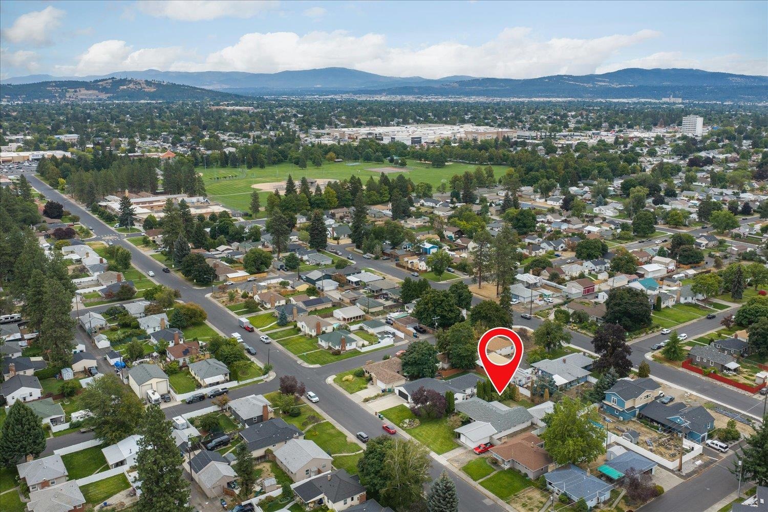 Aerial view of the marked home amid a residential neighborhood, park fields, and distant mountains.