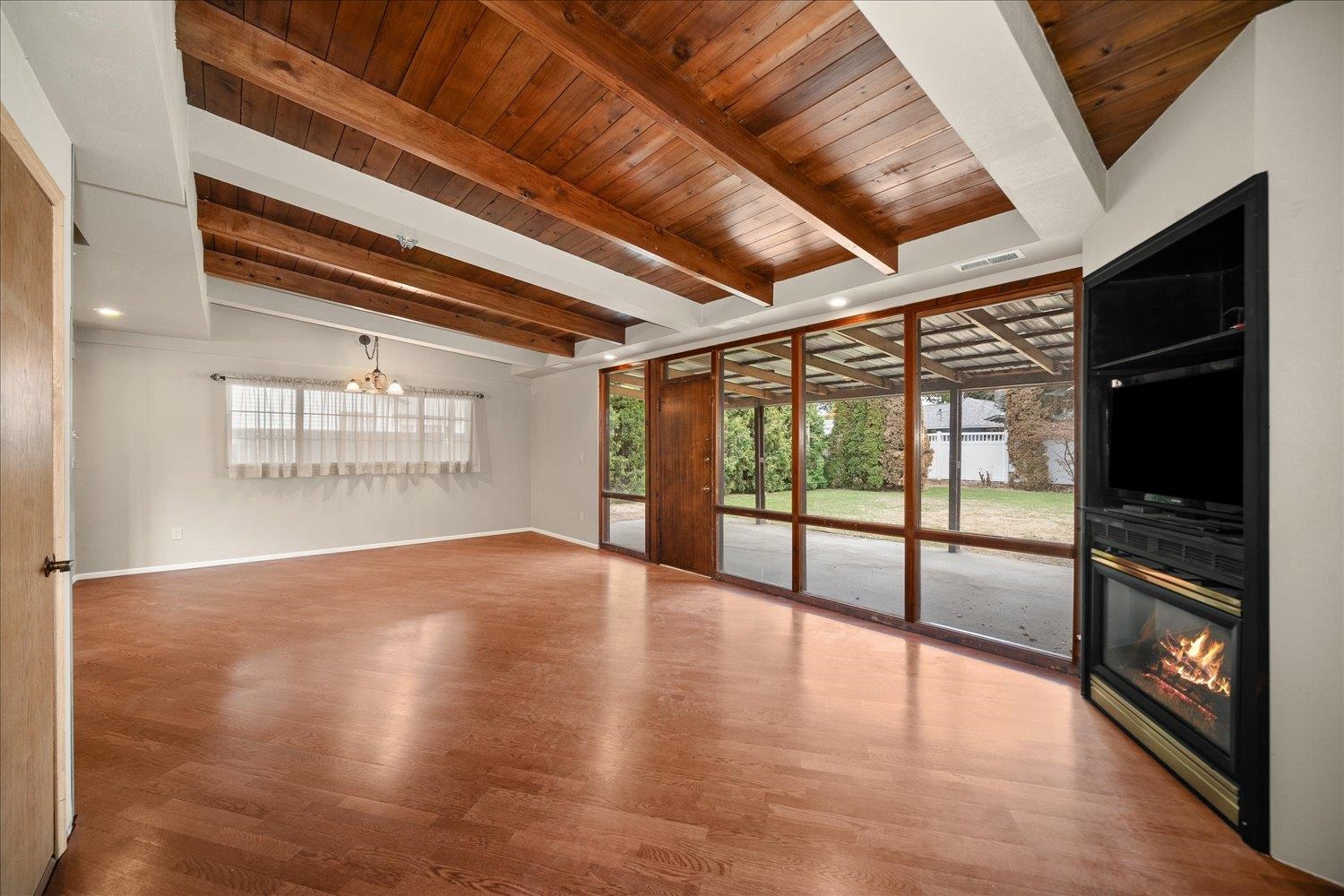 Empty living room with exposed wood ceiling beams, patio-facing glass doors, and a black fireplace.