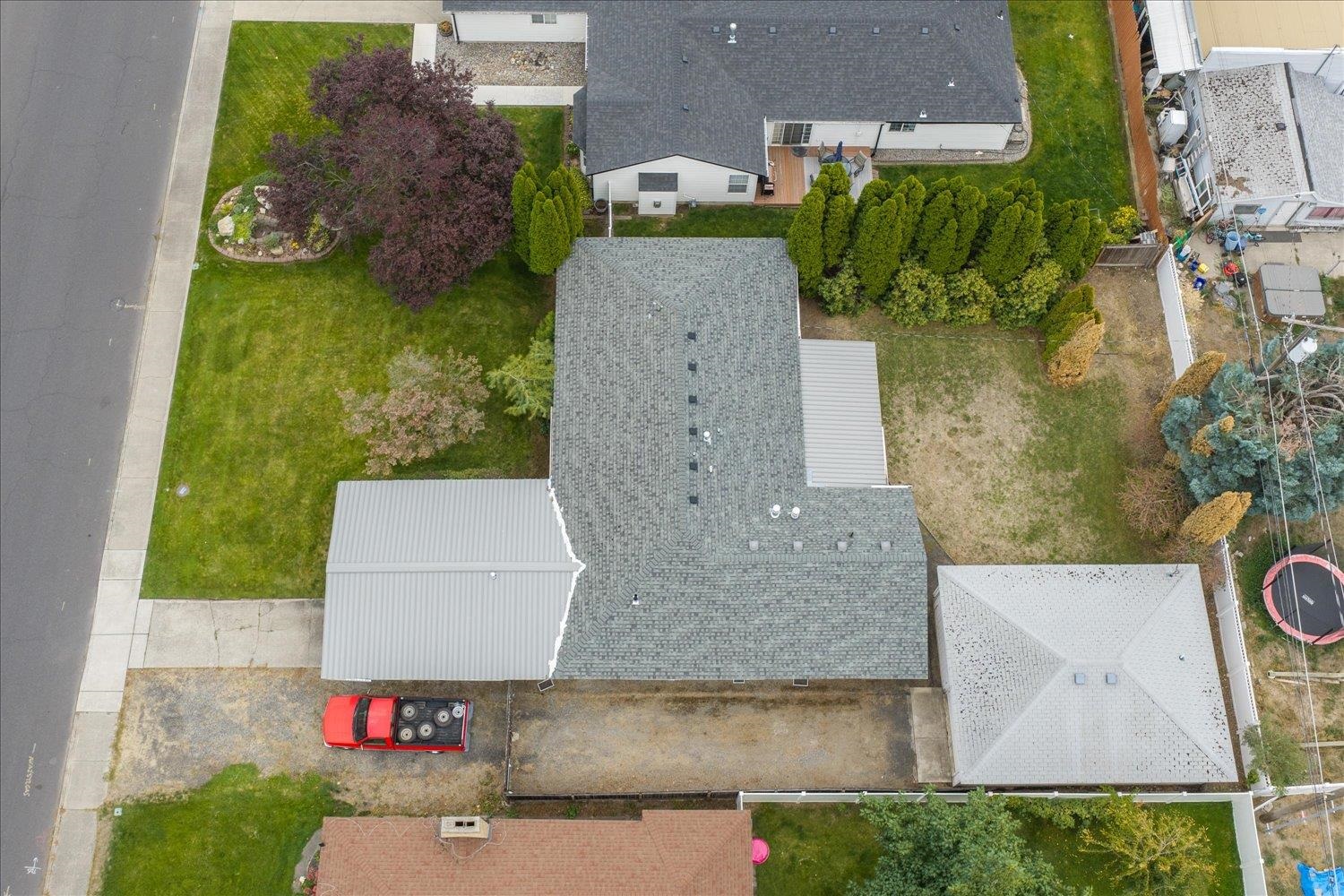 Aerial view of the home, with a gray roof, landscaped front lawn, and fenced backyard.