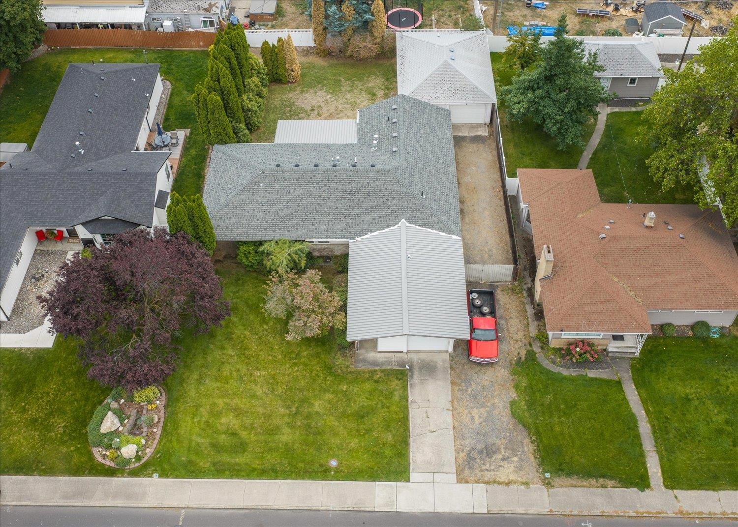 Aerial view of a gray-roofed home, detached garage, landscaped lawn, and gravel driveway.