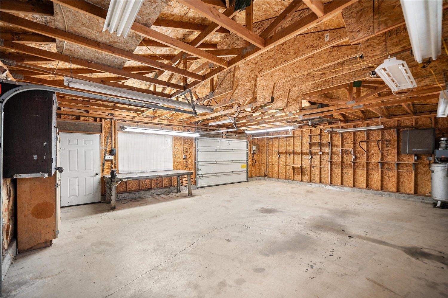 Unfinished garage with exposed roof framing, concrete floor, workbench, and overhead garage door.