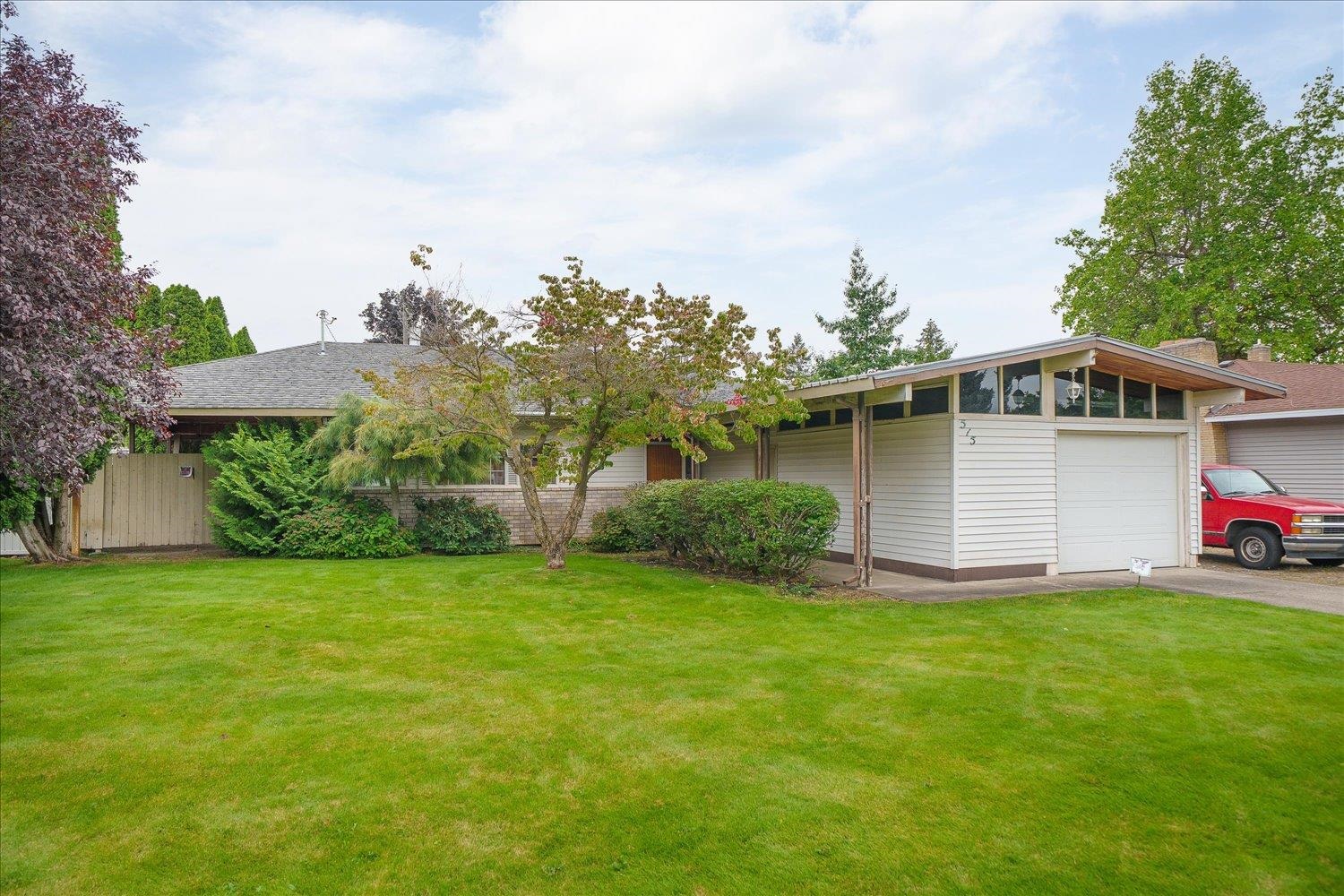 Mid-century modern home with clerestory windows, attached garage, mature trees, and a broad green lawn.
