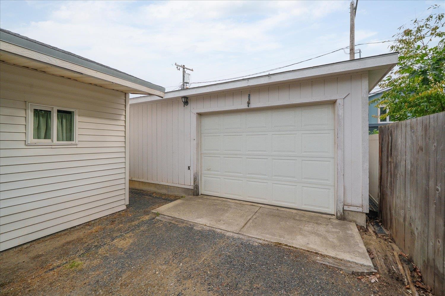 Detached light-colored garage with a white paneled door and concrete driveway beside a house.