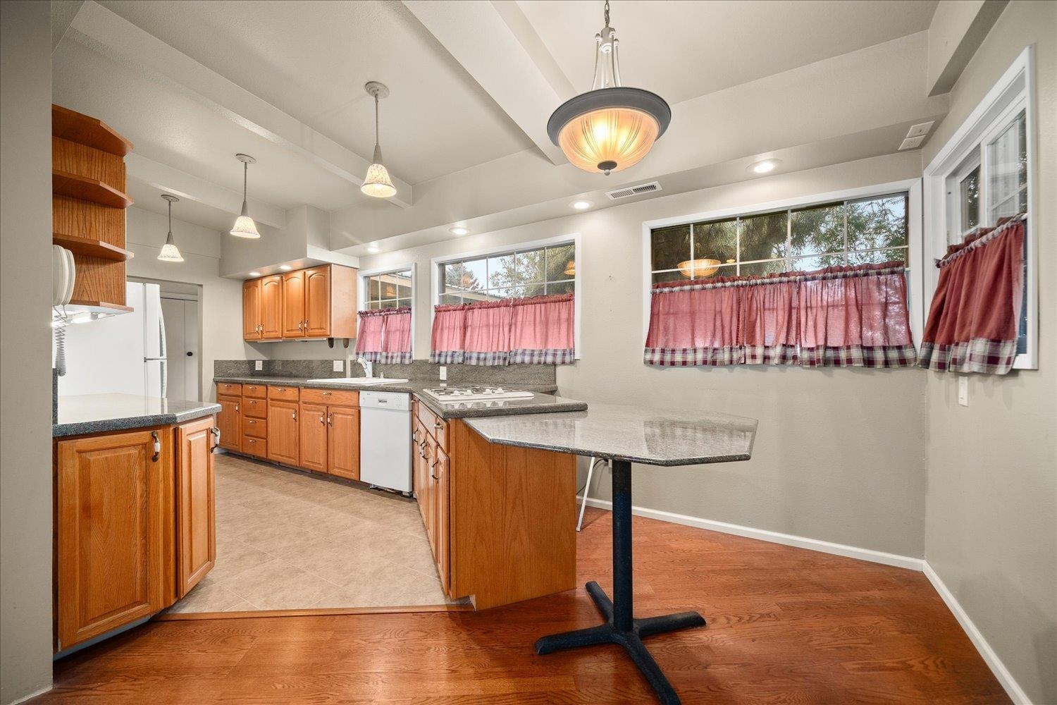 Kitchen with warm wood cabinets, gray countertops, a breakfast bar, and pink plaid window curtains.