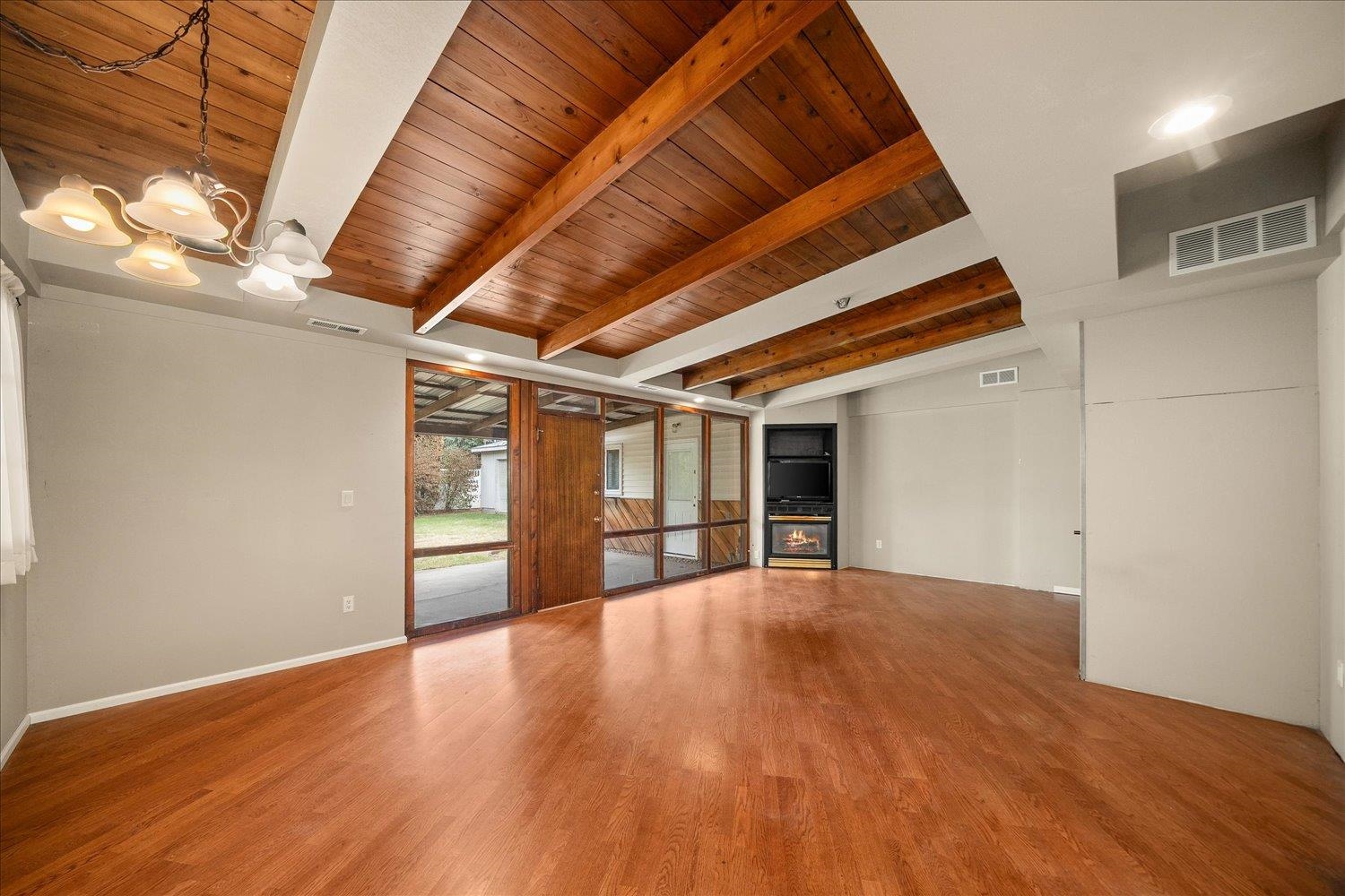 Living room with vaulted wood-beam ceiling, hardwood floors, glass doors, and a gas fireplace.