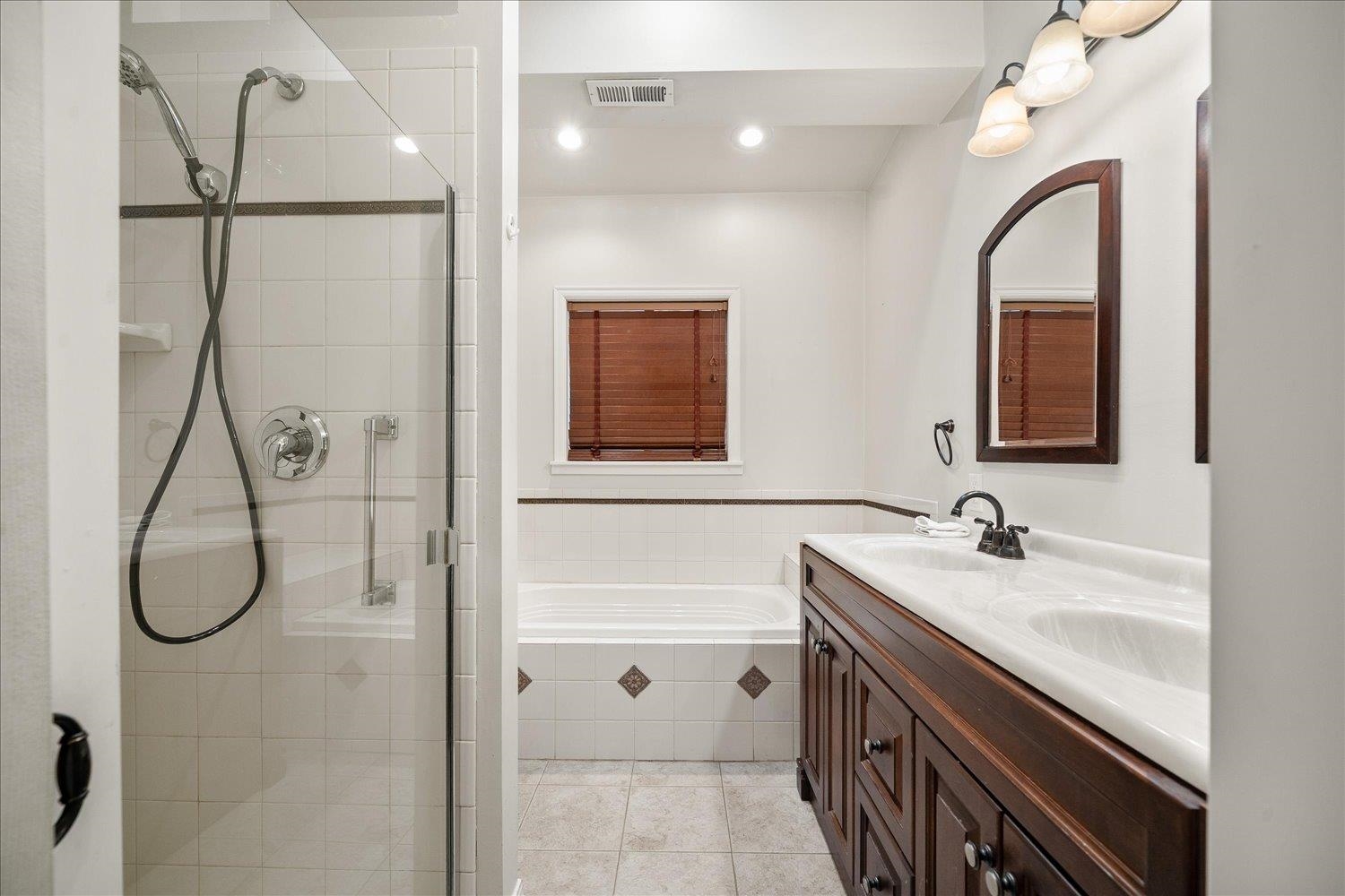 Bathroom with glass shower, built-in tub beneath a window, and dark wood double vanity.