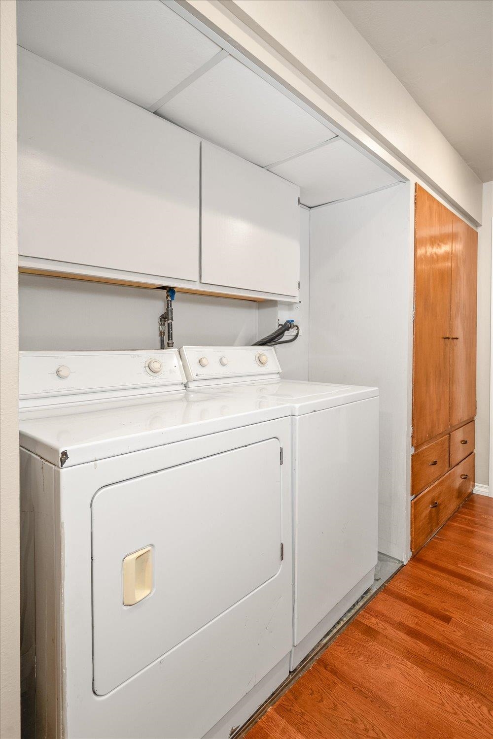Washer and dryer beneath overhead cabinets beside a wooden storage cabinet.