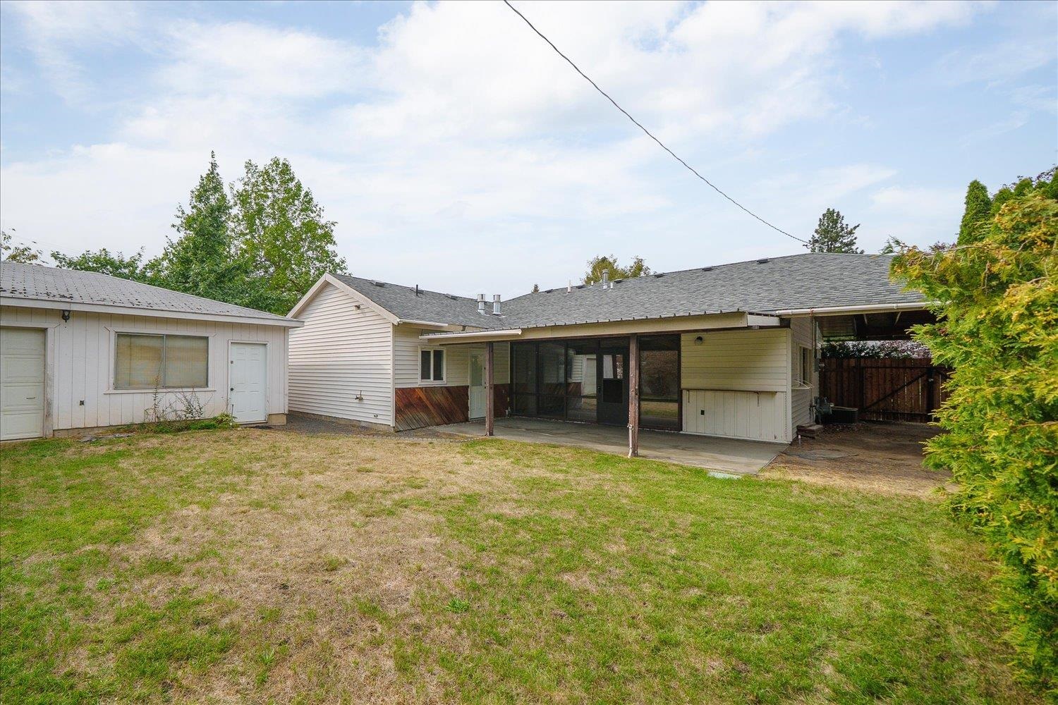 Rear of a single-story house with a screened patio and broad patchy lawn.