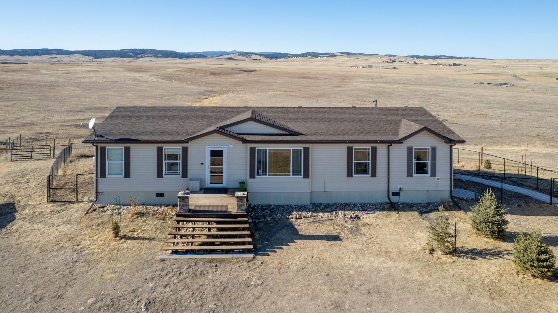 Single-story ranch home with front steps on open rural land, with rolling hills in the distance.
