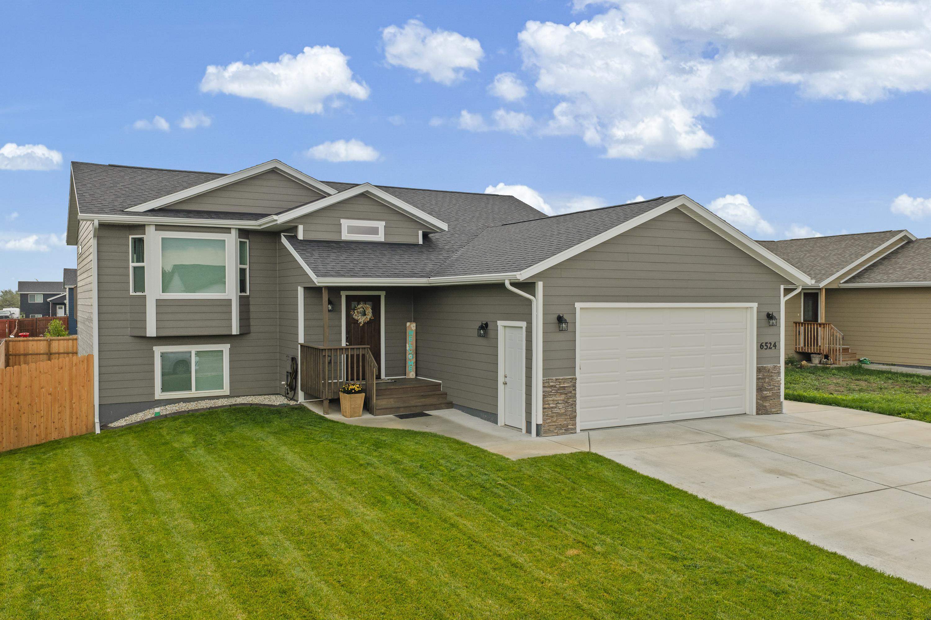 Gray two-story house with a covered porch, attached garage, and broad green lawn.