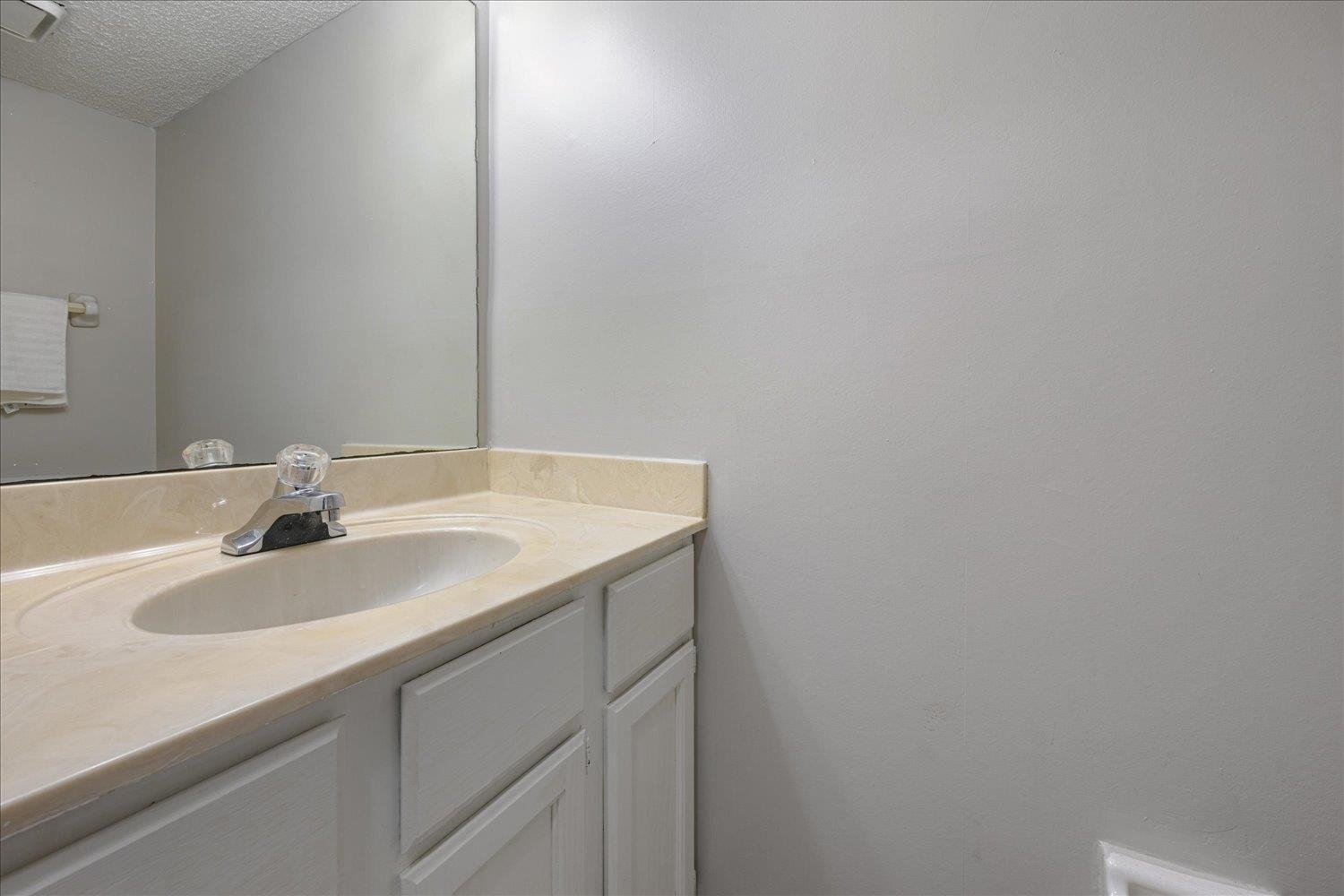 Bathroom vanity with an oval sink, cream countertop, chrome faucet, and large mirror.