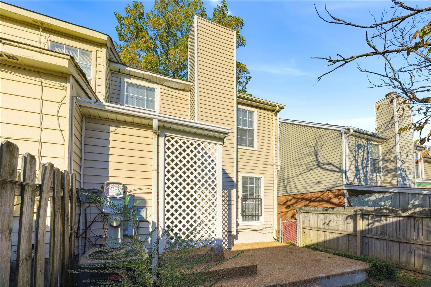 Rear exterior of a beige two-story home with a white lattice screen and fenced paved patio.