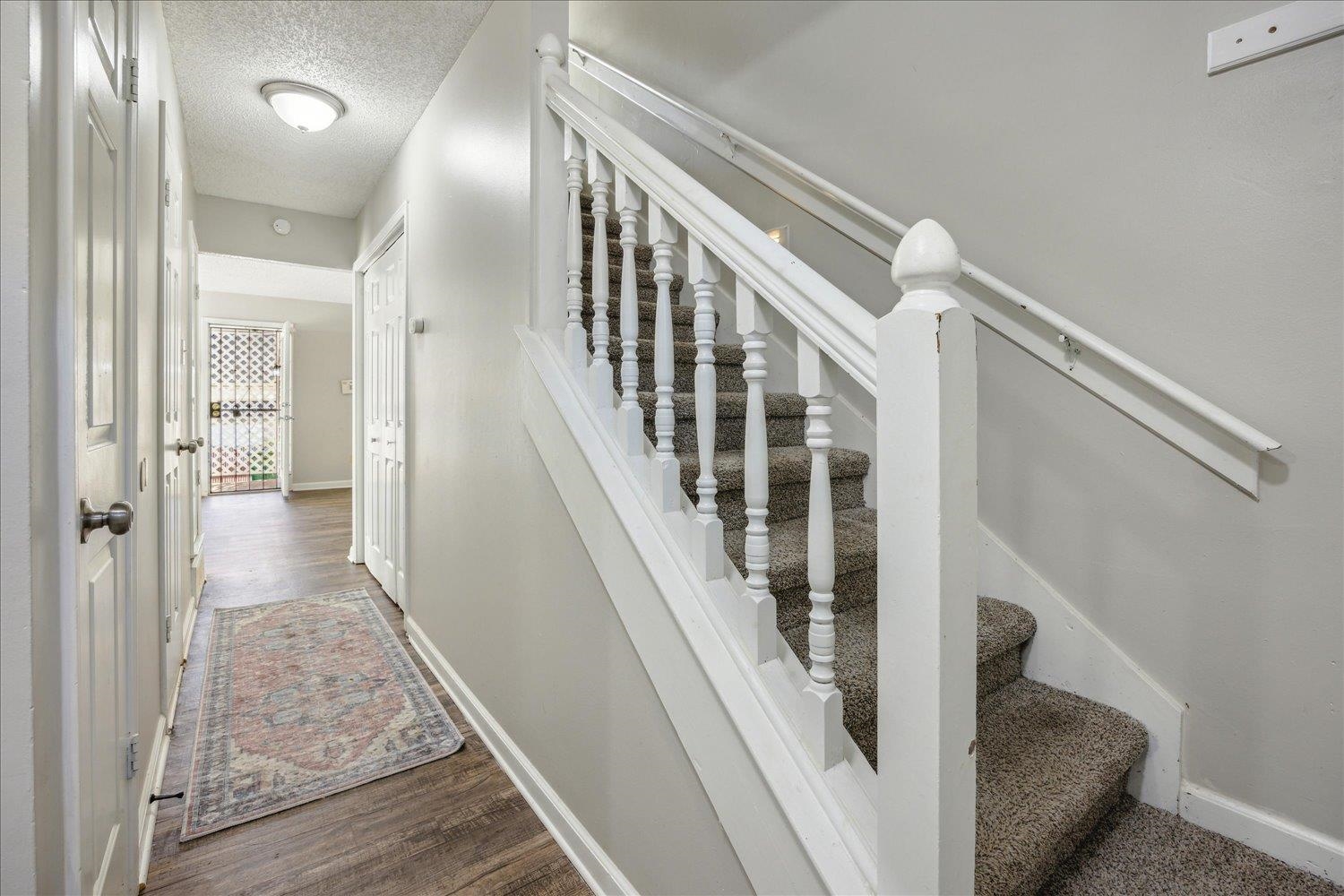 Hallway with a patterned runner and carpeted staircase with white railings.