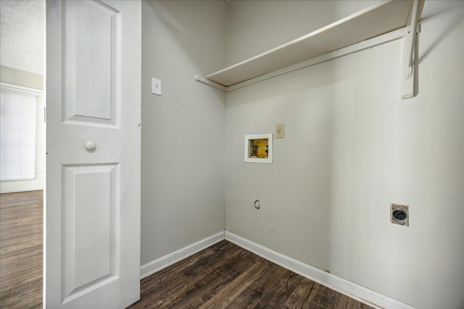 Empty laundry room with washer and dryer hookups, a raised shelf, and dark wood-look flooring.