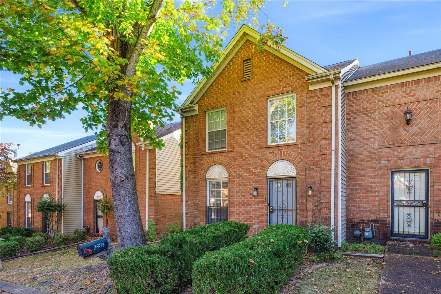 Red-brick townhouse with a steep gable, arched windows, and a large tree in front.
