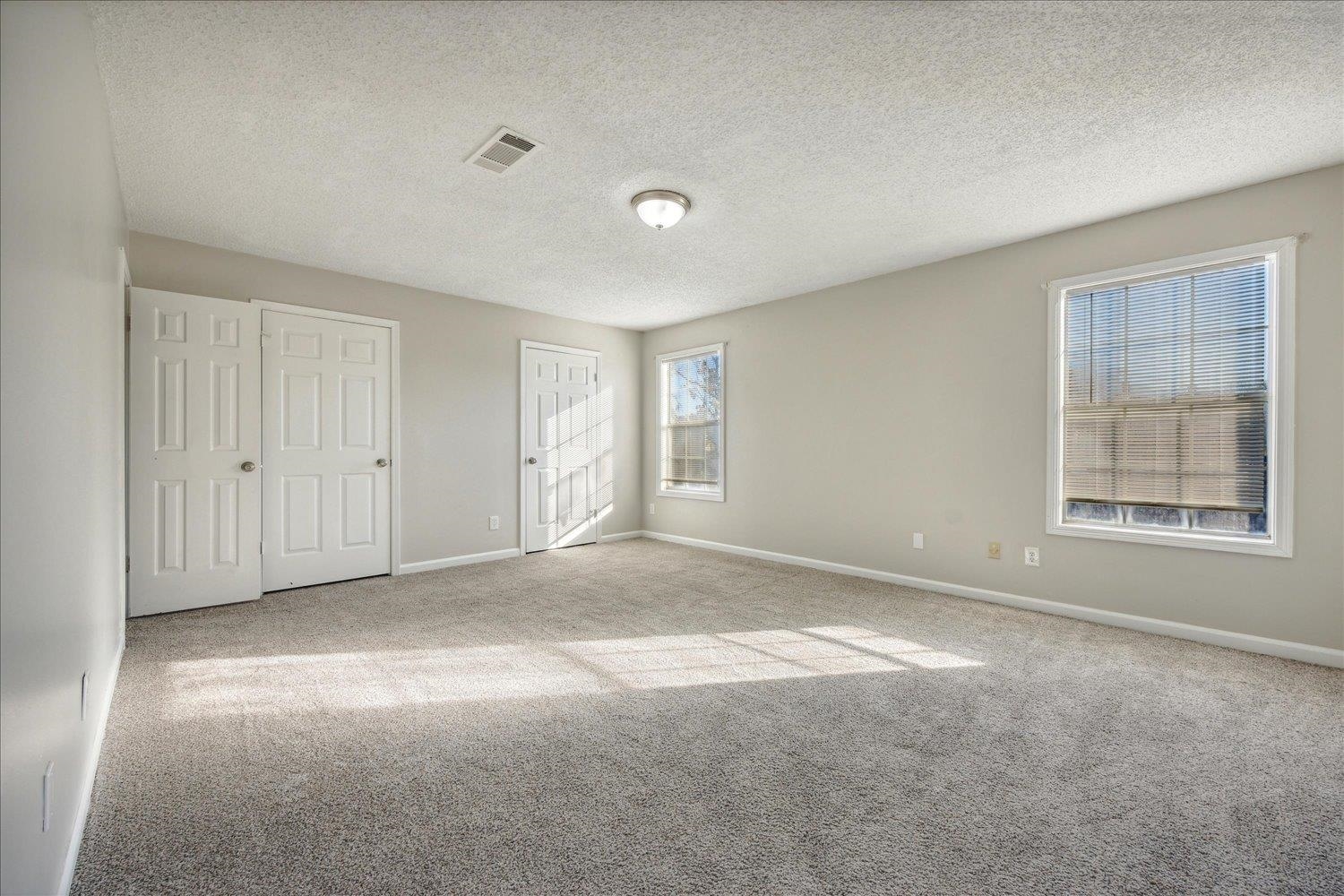 Empty carpeted bedroom with two windows and white closet doors.