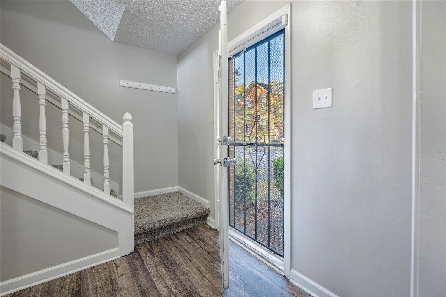 Entryway with a carpeted staircase, wood-look flooring, and an open metal security screen door.