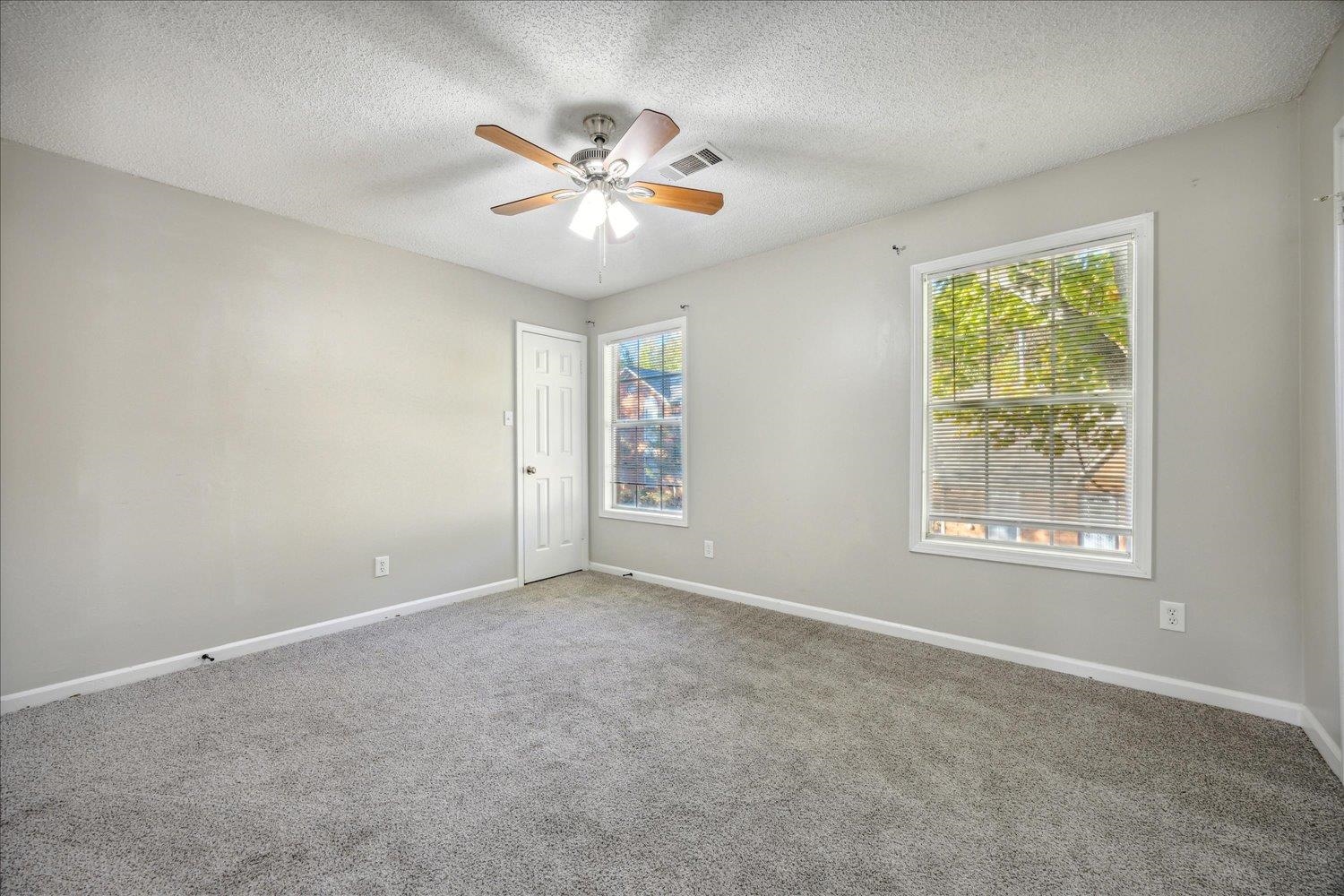Vacant bedroom with gray carpet, two windows, and a ceiling fan.
