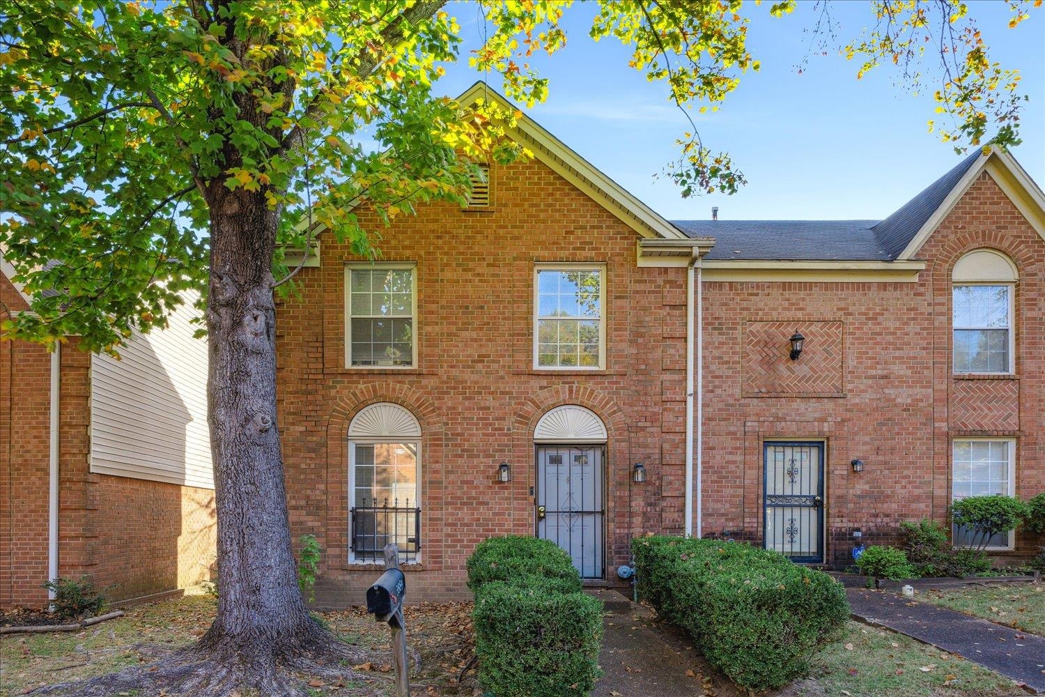 Two-story brick townhouse with arched windows, entryways, and a large tree in front.