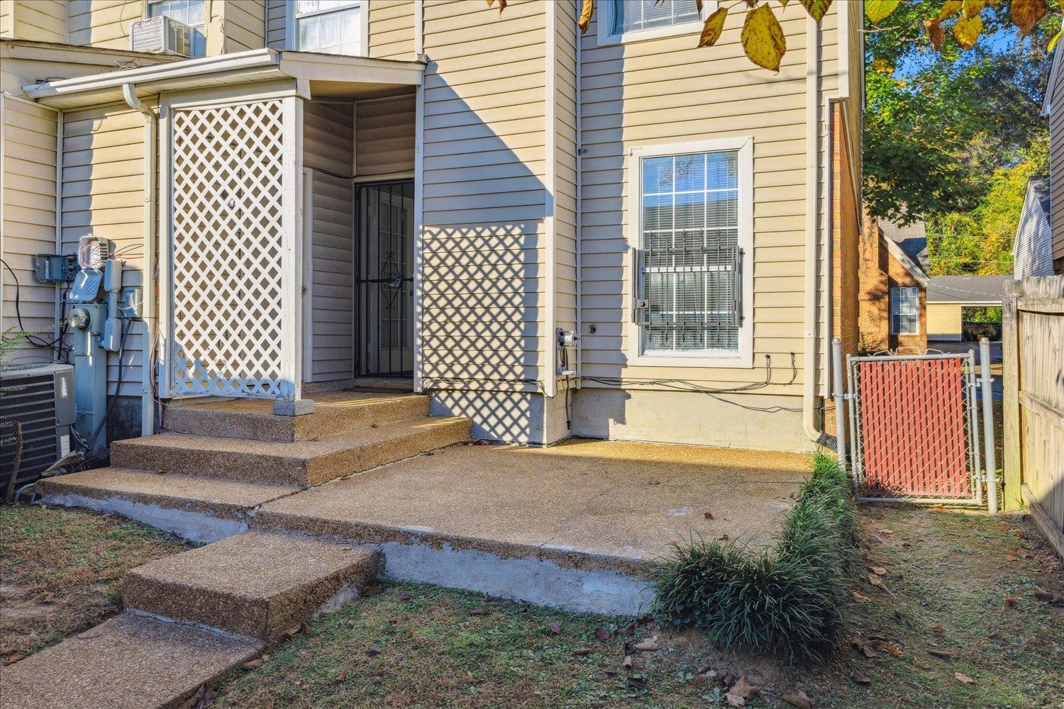 Beige-sided home exterior with concrete patio steps, lattice screening, and a barred window.