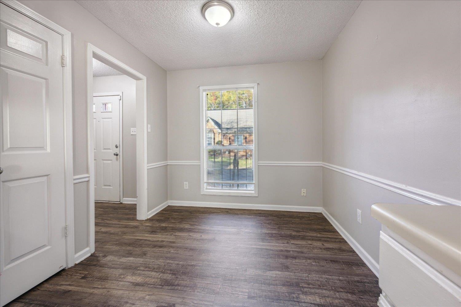 Empty room with dark wood-look flooring, white chair rail, and a window with blinds.