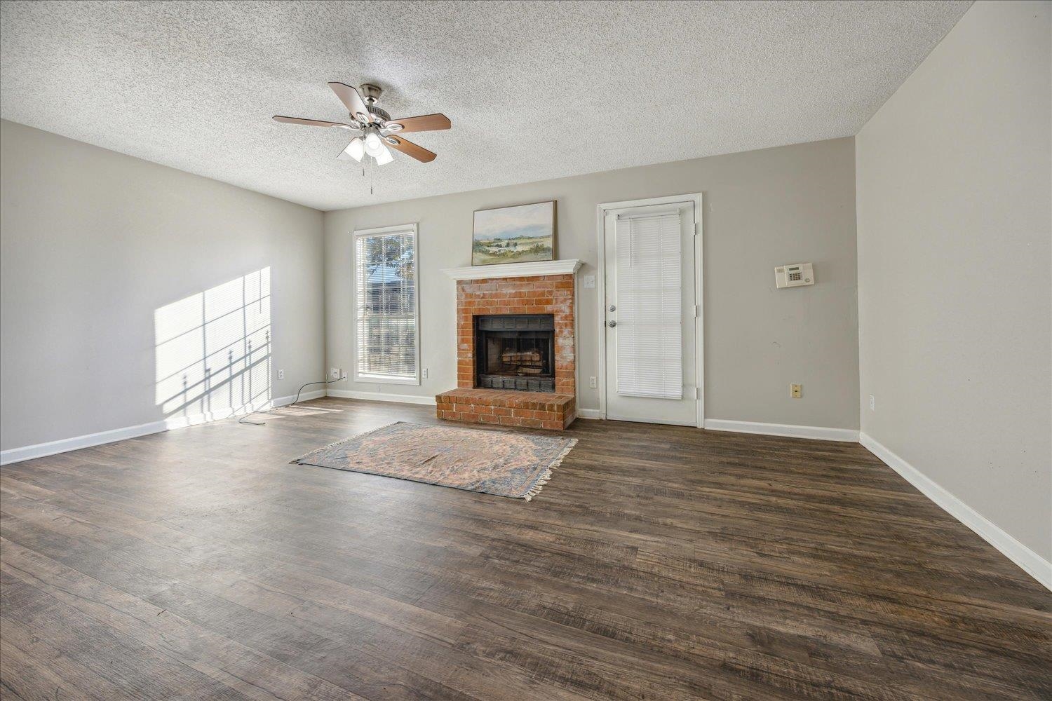 Living room with dark wood floors, a brick fireplace, and sunlight across the wall.