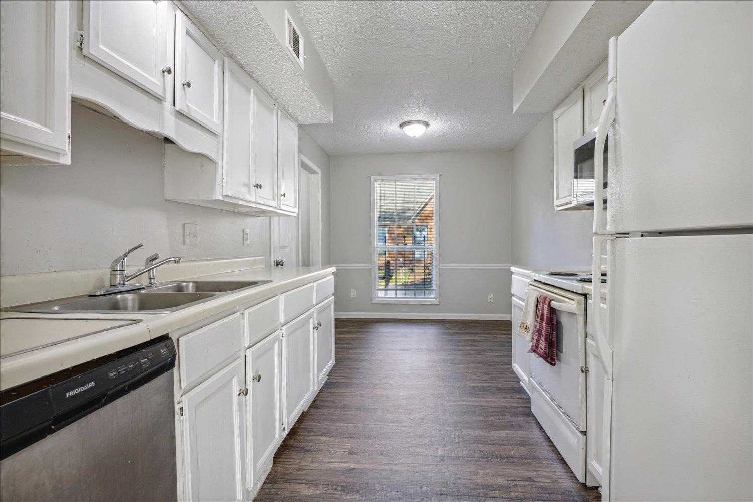 Galley kitchen with white cabinets, a double sink, and dark wood-look flooring.