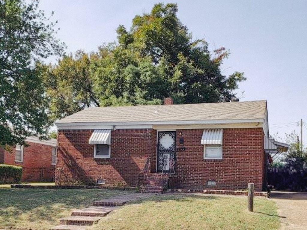 Single-story red brick house with striped window awnings and front steps across a grassy lawn.