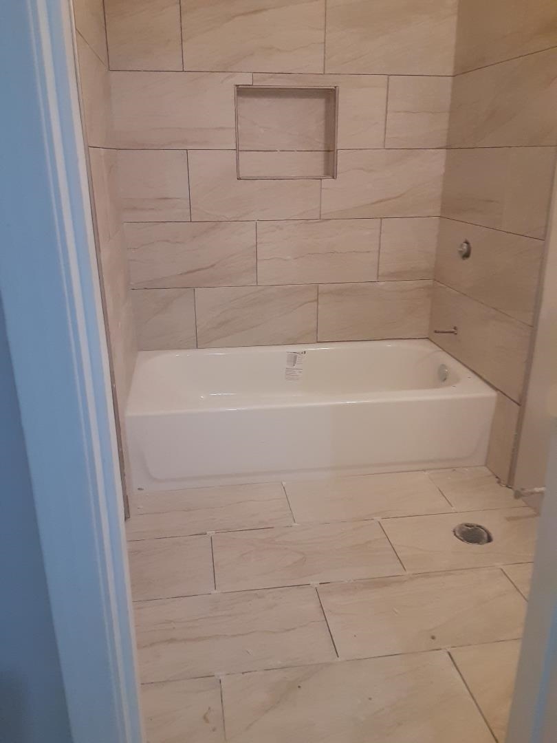 Bathroom with a white bathtub and beige tiled surround with a recessed niche.