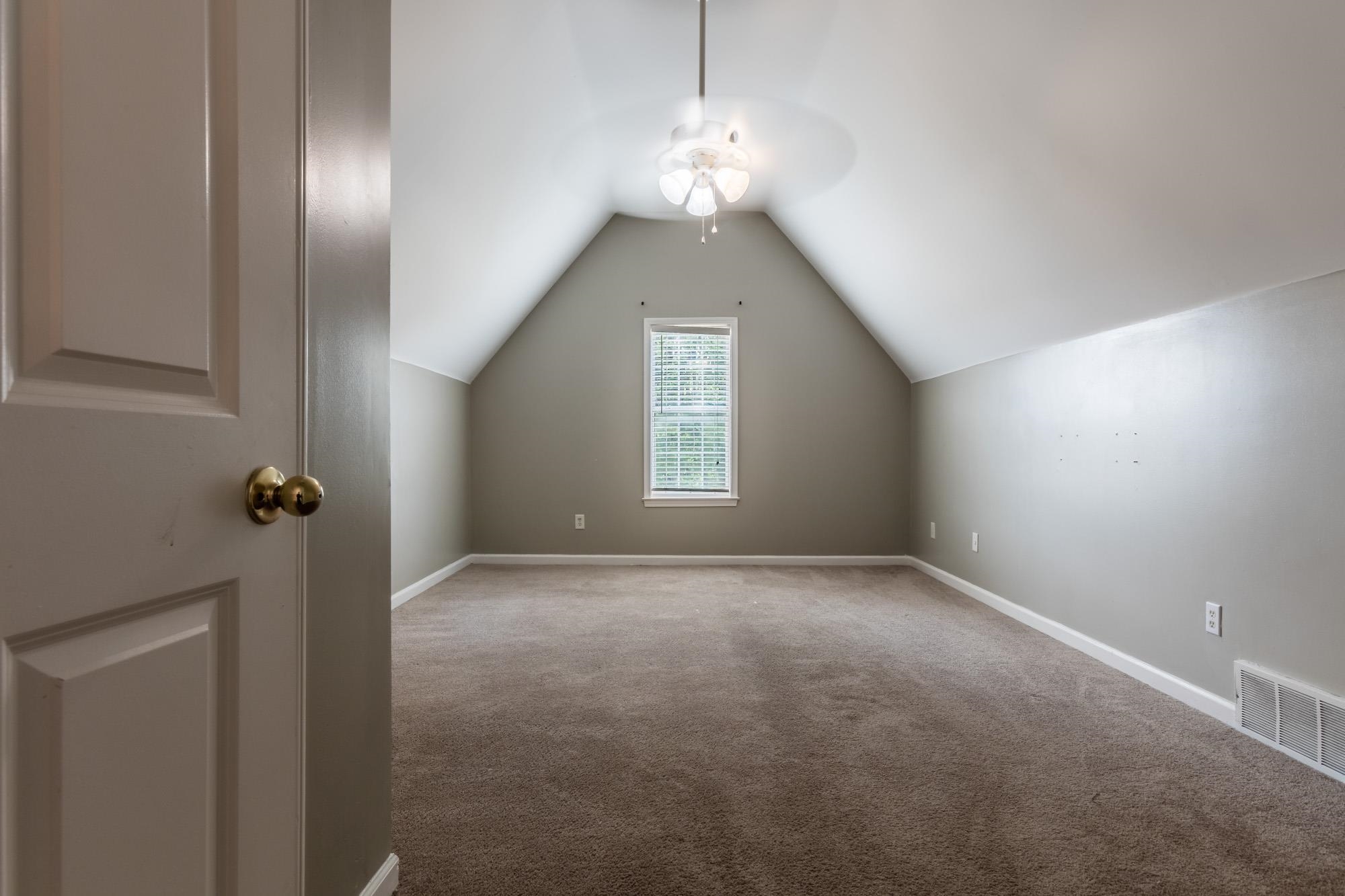 Empty bedroom with a vaulted ceiling, beige carpet, and a window with blinds.