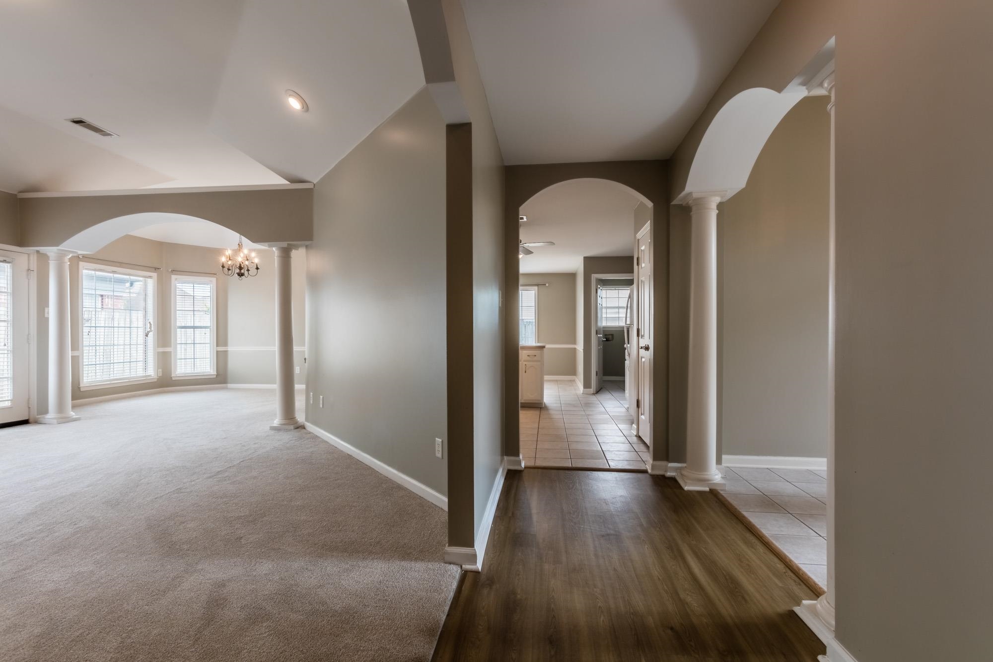 Vacant living area with tall windows, a chandelier, decorative arches, and a wood-floored entry.