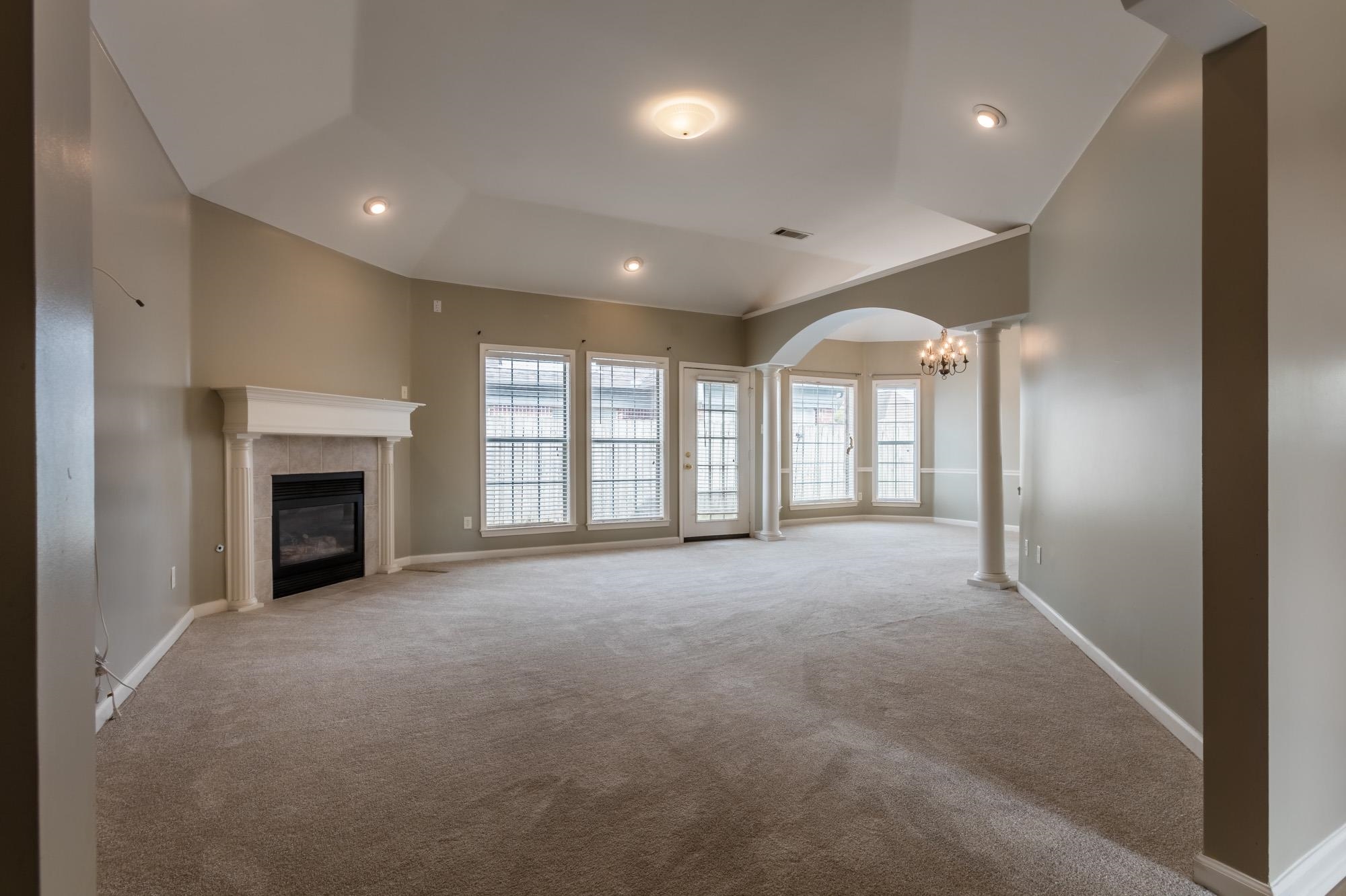 Empty living room with a fireplace, vaulted ceiling, and arched opening to a windowed sitting area.