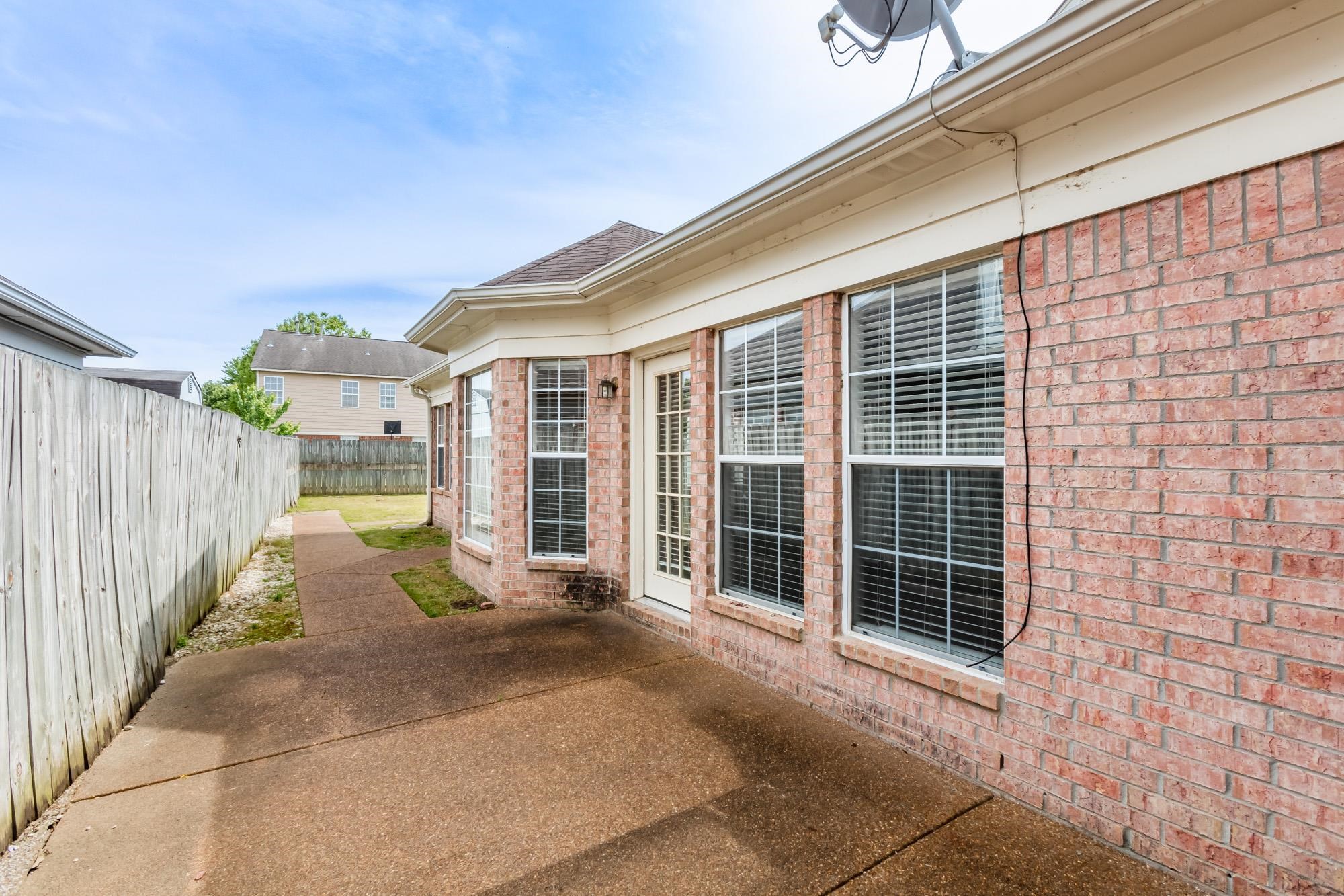Brick house with a broad concrete patio and a wooden privacy fence along the side yard.