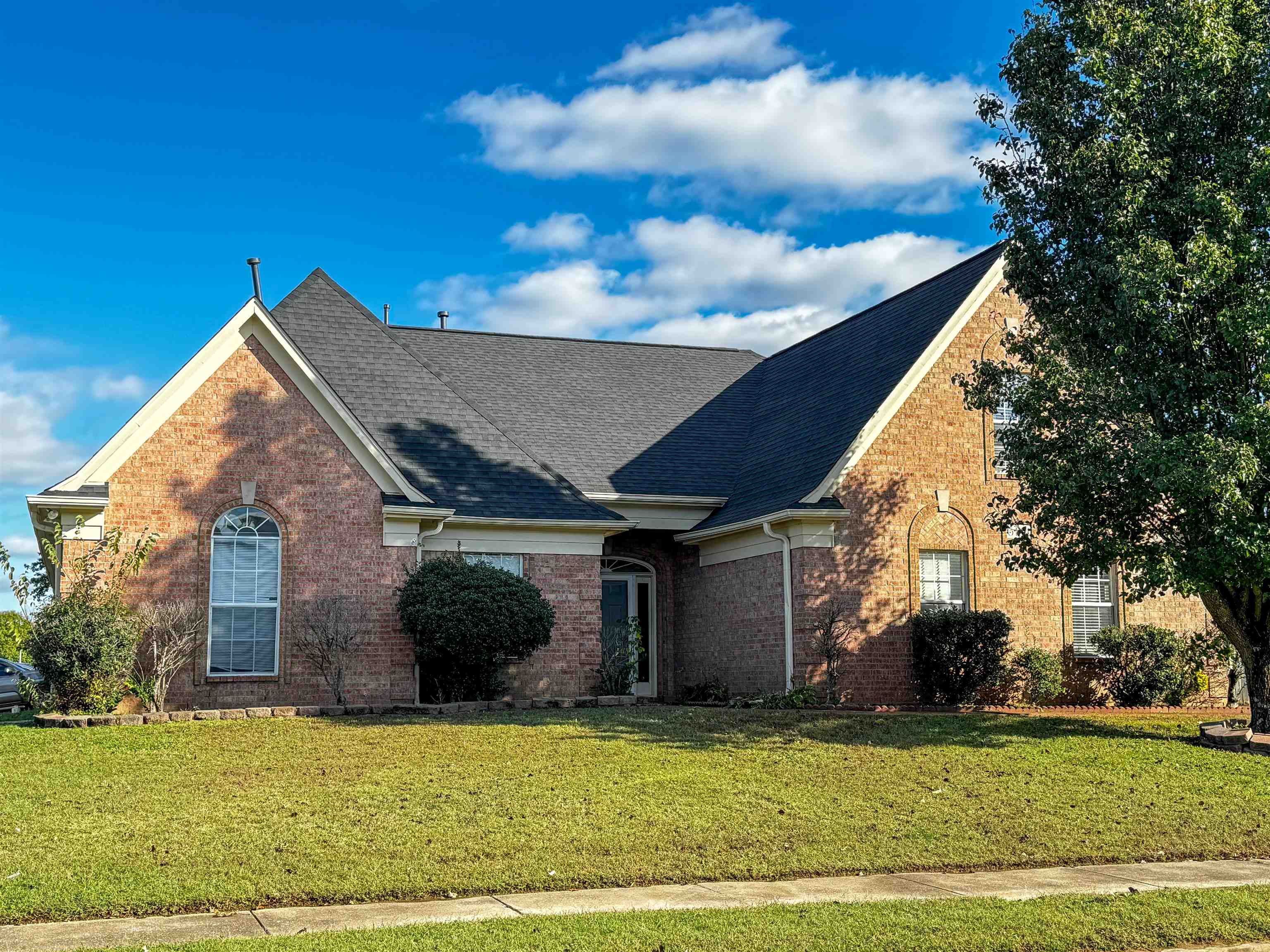 Red-brick home with steep gray gabled roofs, arched windows, and a broad front lawn.