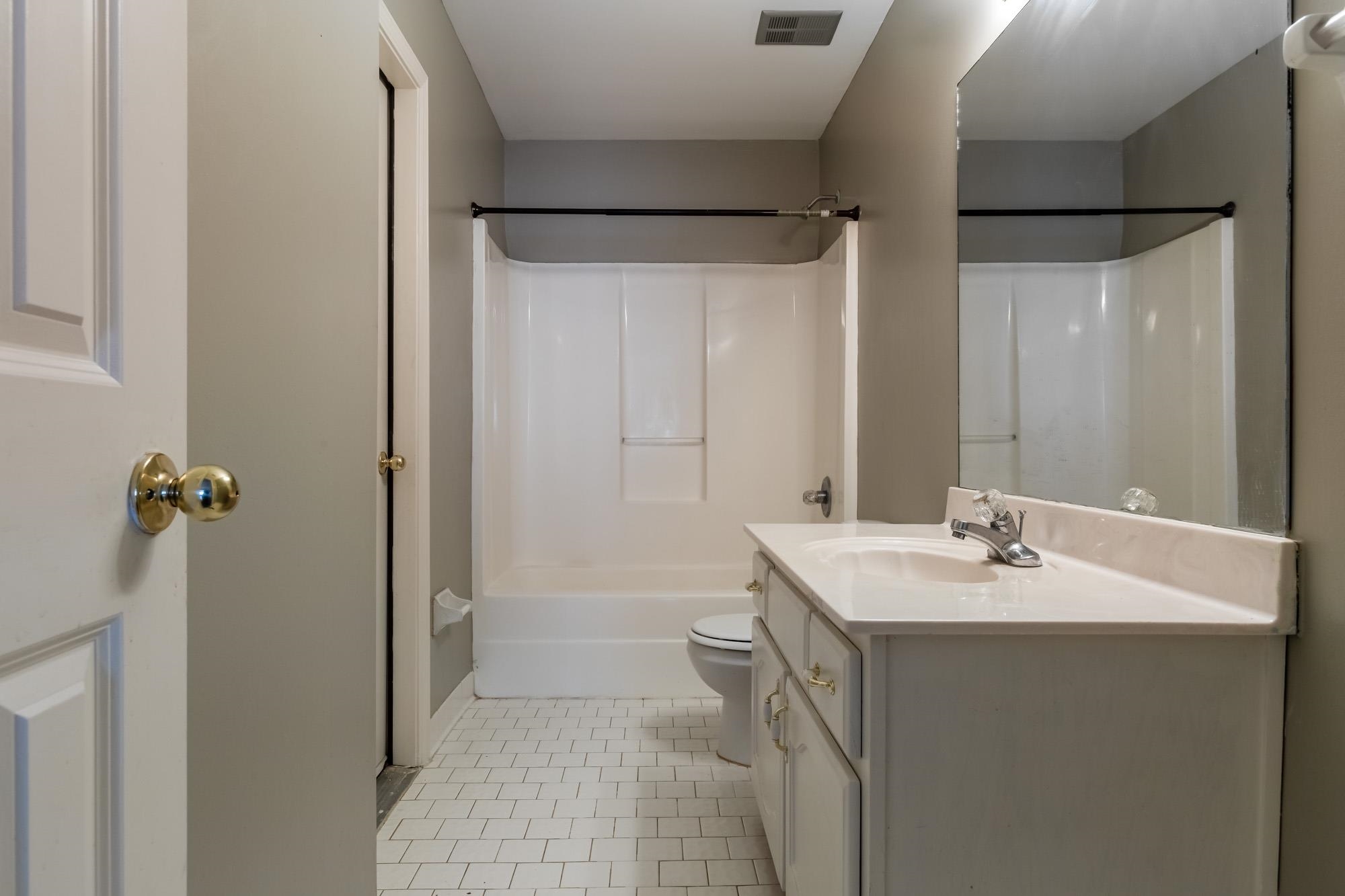 Bathroom with a white tub and shower, tiled floor, toilet, and mirrored vanity.