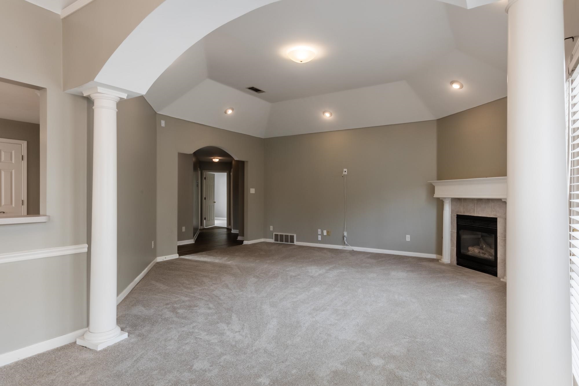 Empty living room with vaulted ceiling, white columns, gray carpet, and a fireplace.