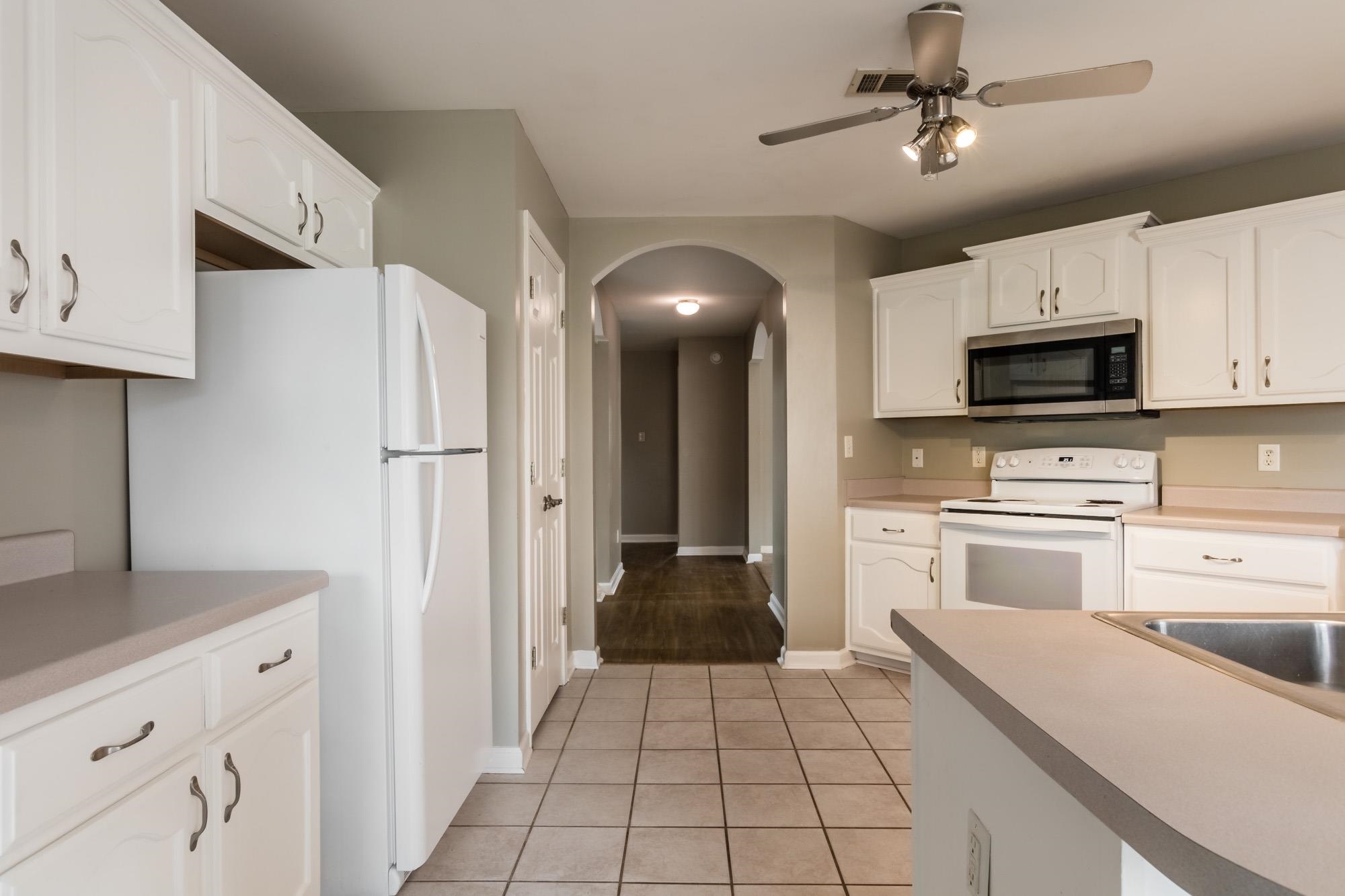 Kitchen with white cabinets and appliances, tiled floor, and an arched hallway opening.