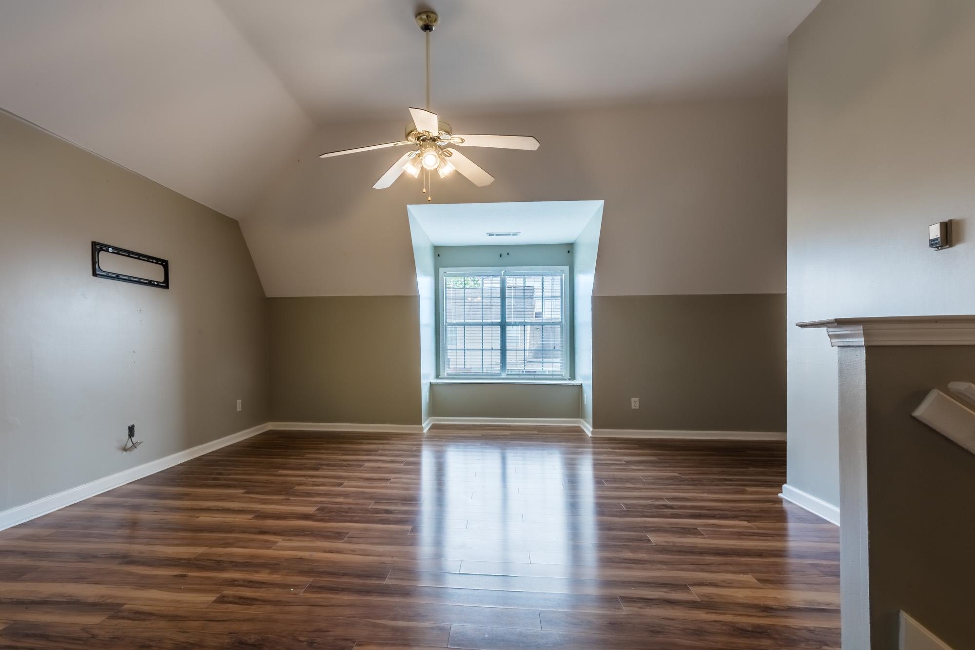 Empty room with dark wood flooring, a ceiling fan, and a recessed window alcove with blinds.
