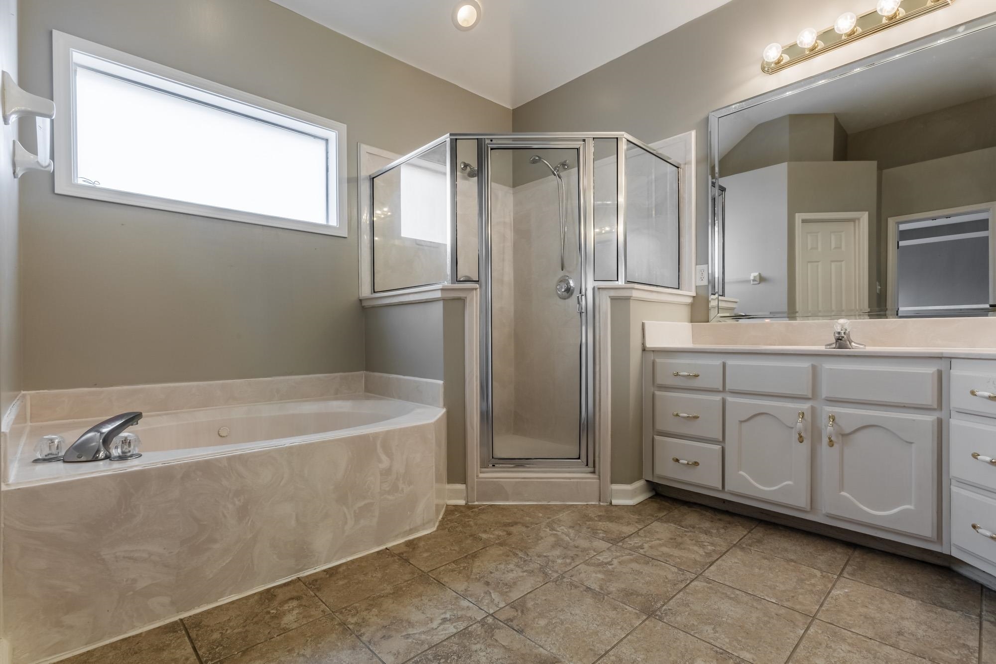 Bathroom with a corner glass shower, built-in soaking tub, and long white vanity.